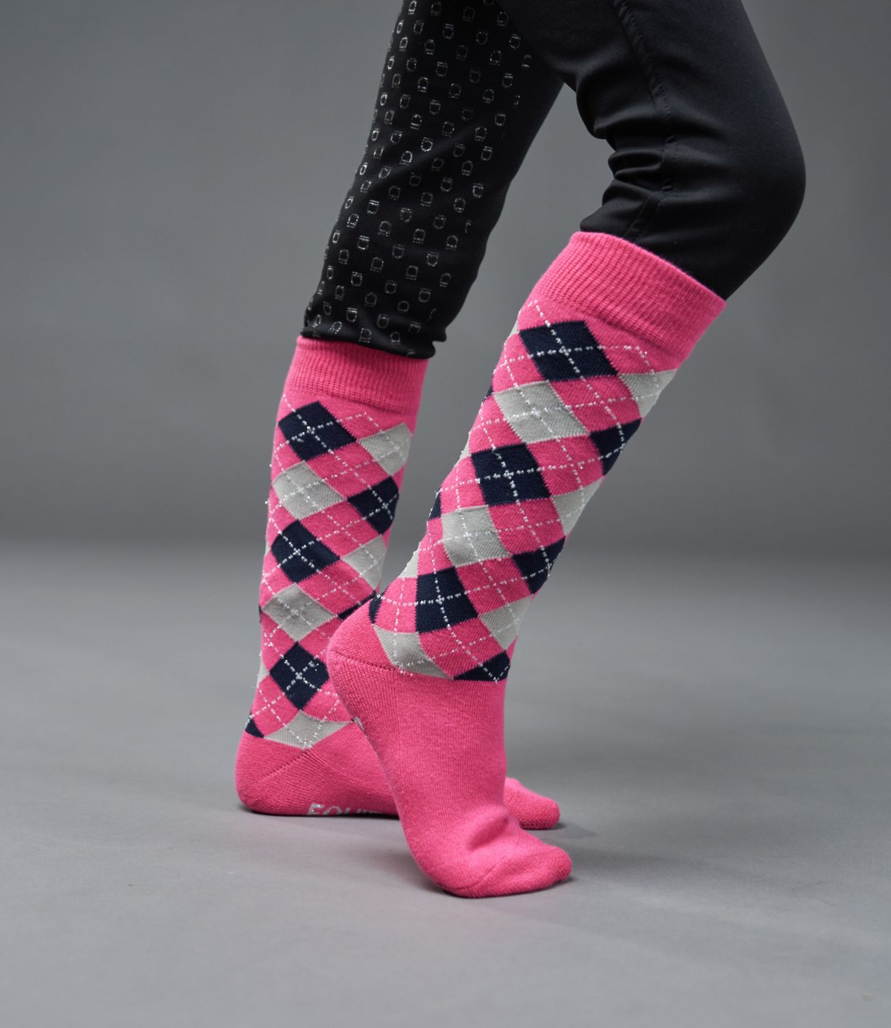 Pink argyle socks worn with black pants on a gray background