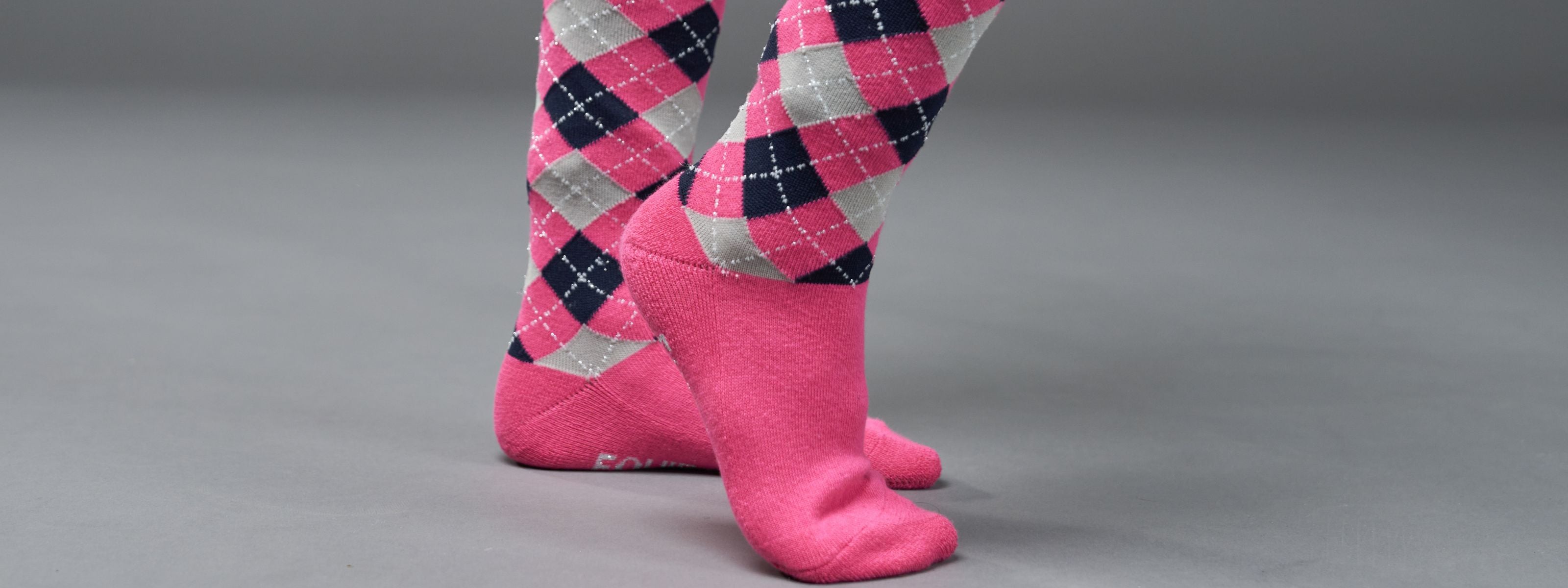 Pink argyle socks worn on a gray background