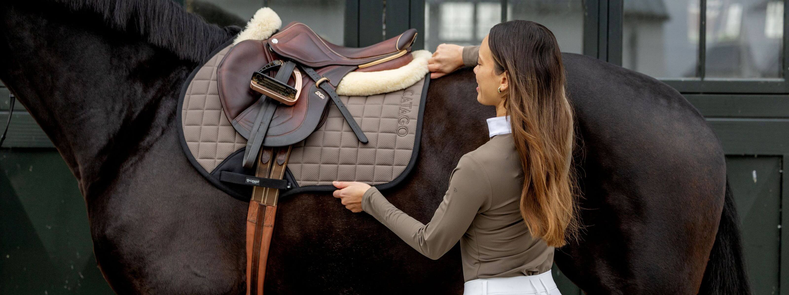 Woman adjusting a saddle on a horse in an outdoor setting