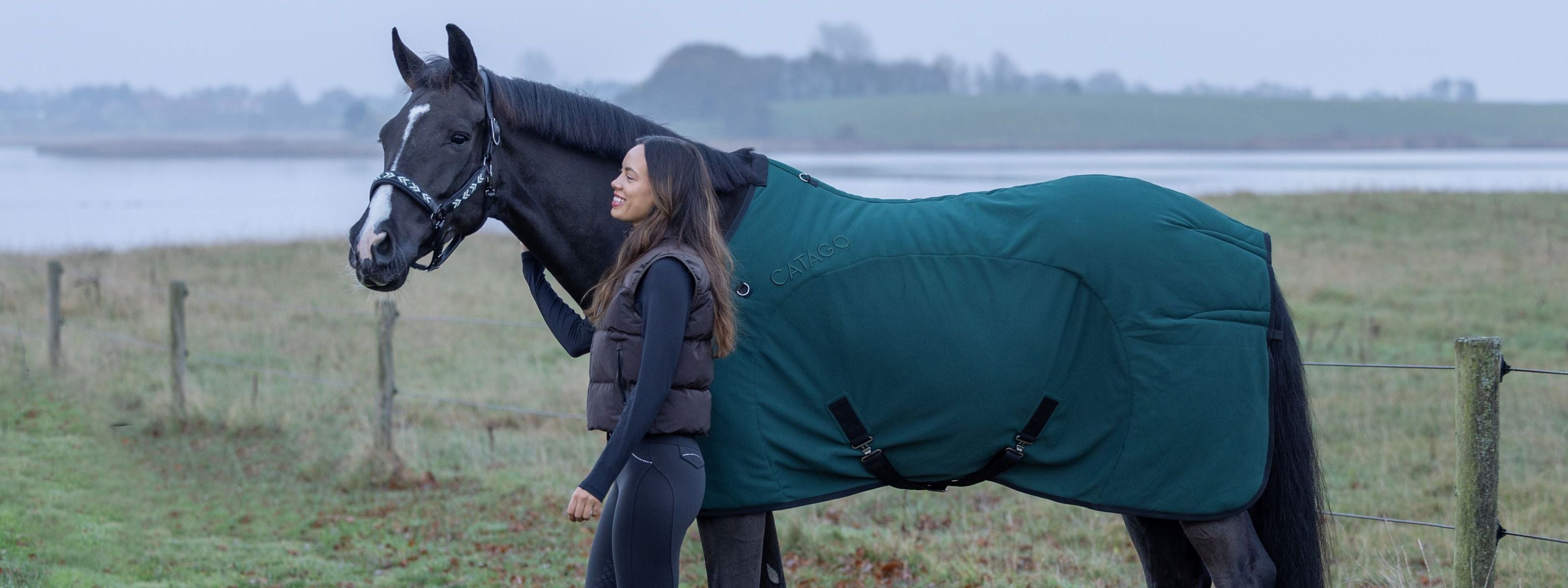 Woman standing next to a horse wearing a green blanket in a field.