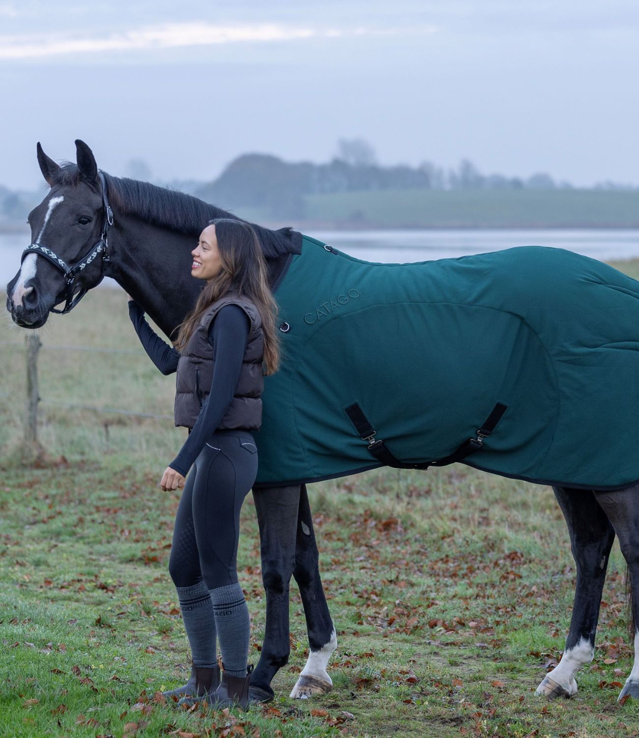 Woman standing next to a horse wearing a green rug in a field