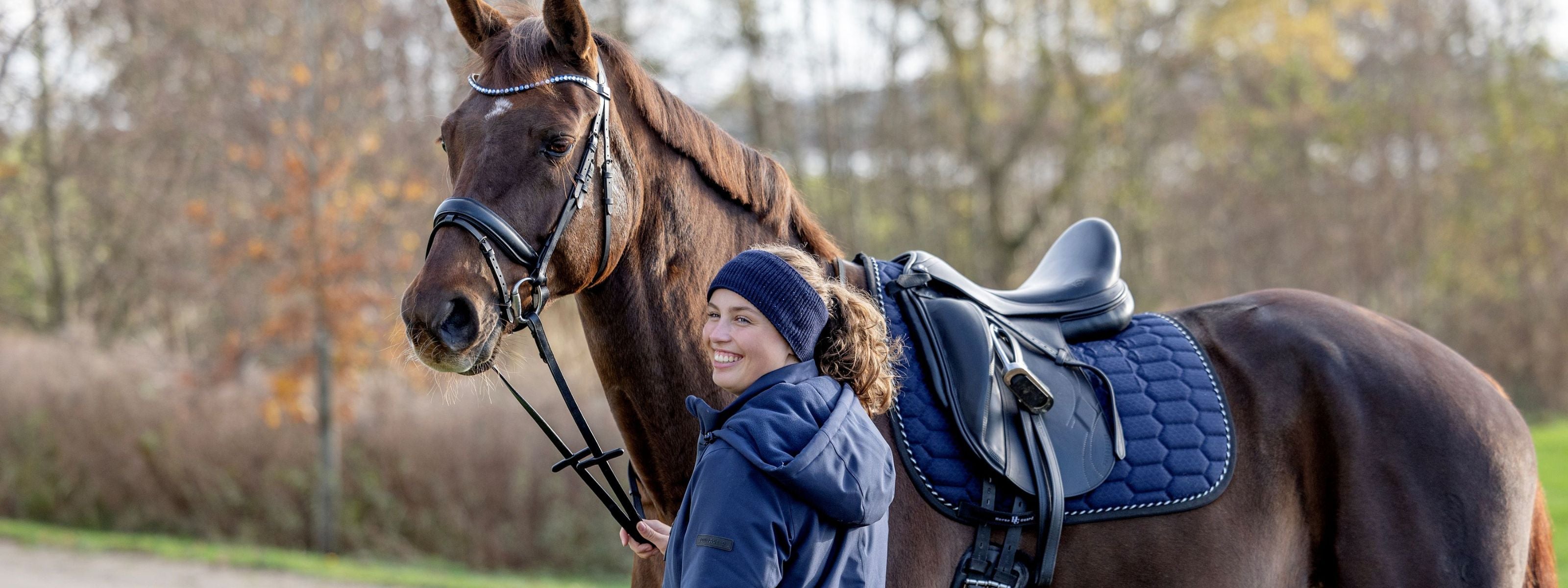 Woman standing next to a horse with a blue saddle pad in an outdoor setting