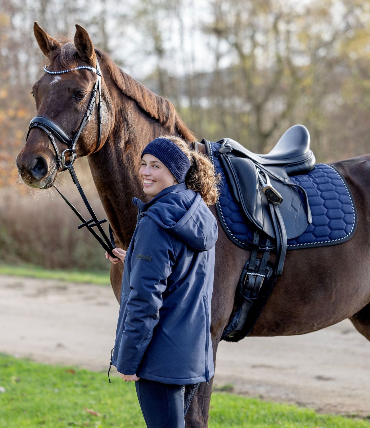 Woman standing next to a horse with a blue saddle pad in an outdoor setting
