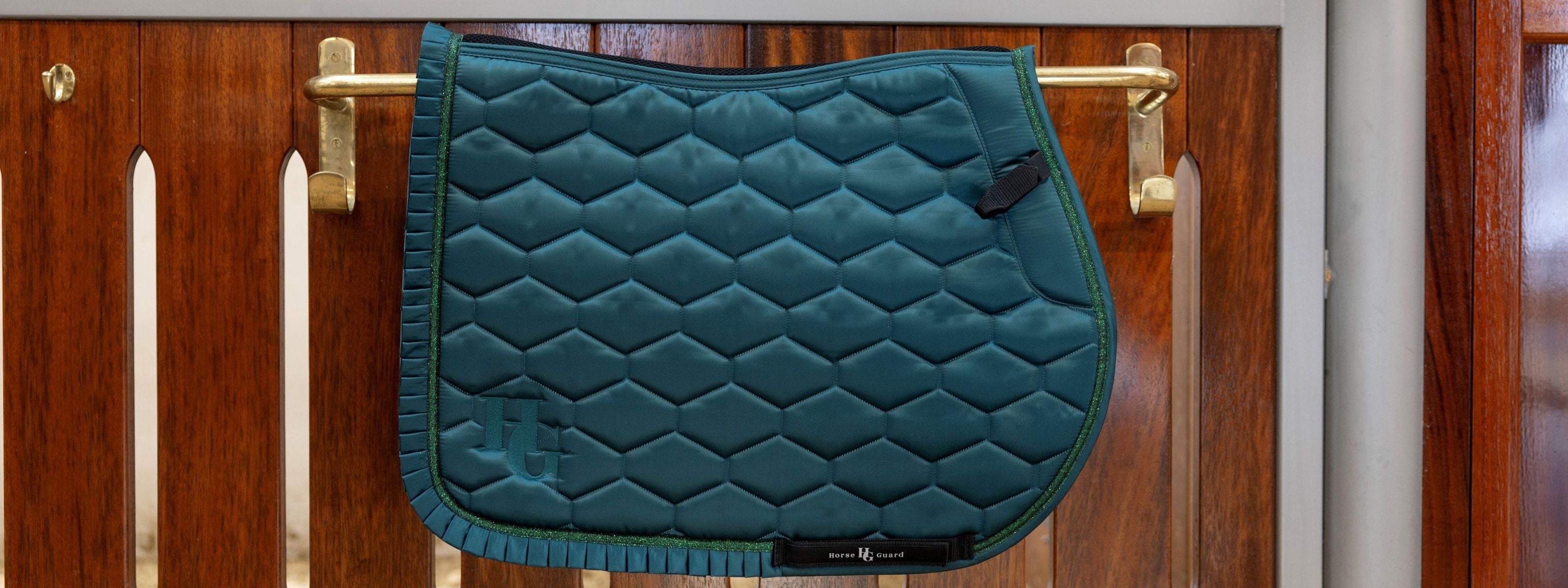 Teal quilted saddle pad on a wooden horse stable door.