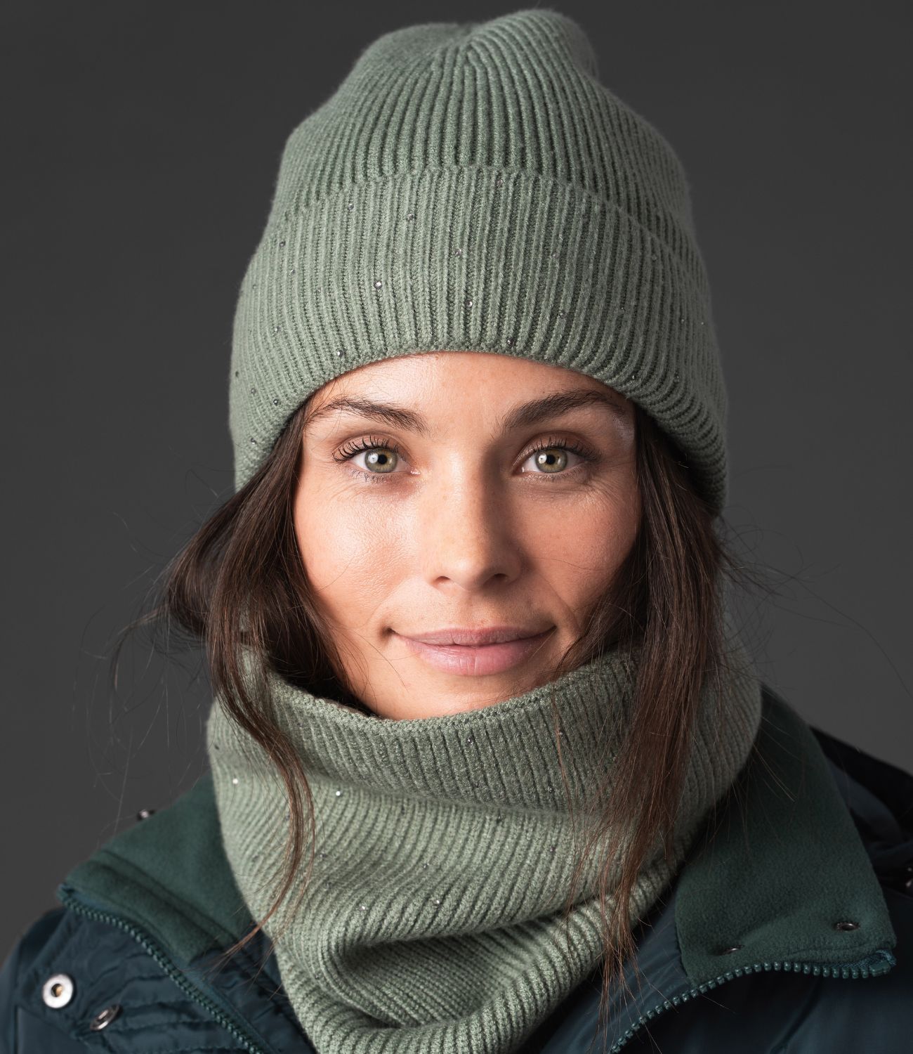 Woman wearing a green knit beanie and scarf against a dark background