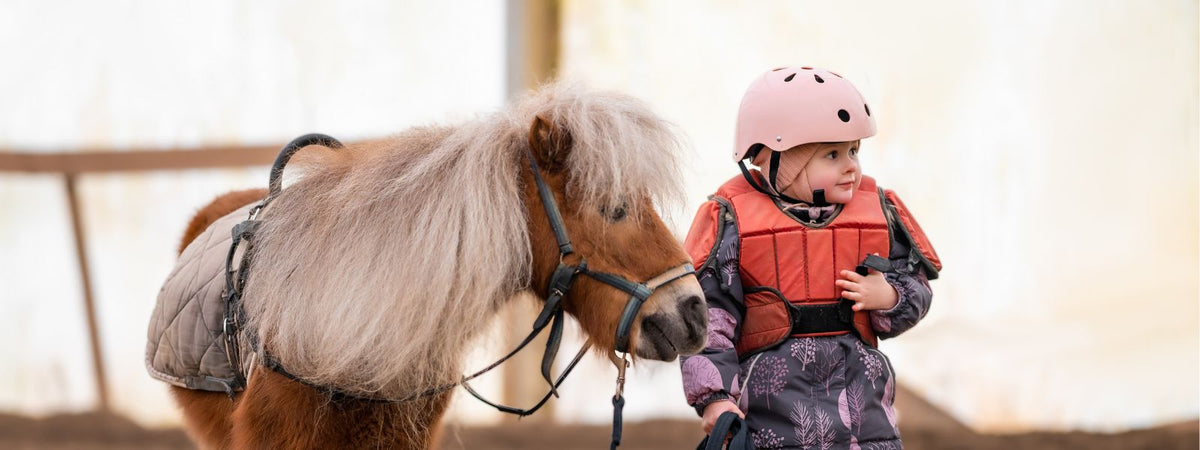 Small child with riding gear standing next to a small pony