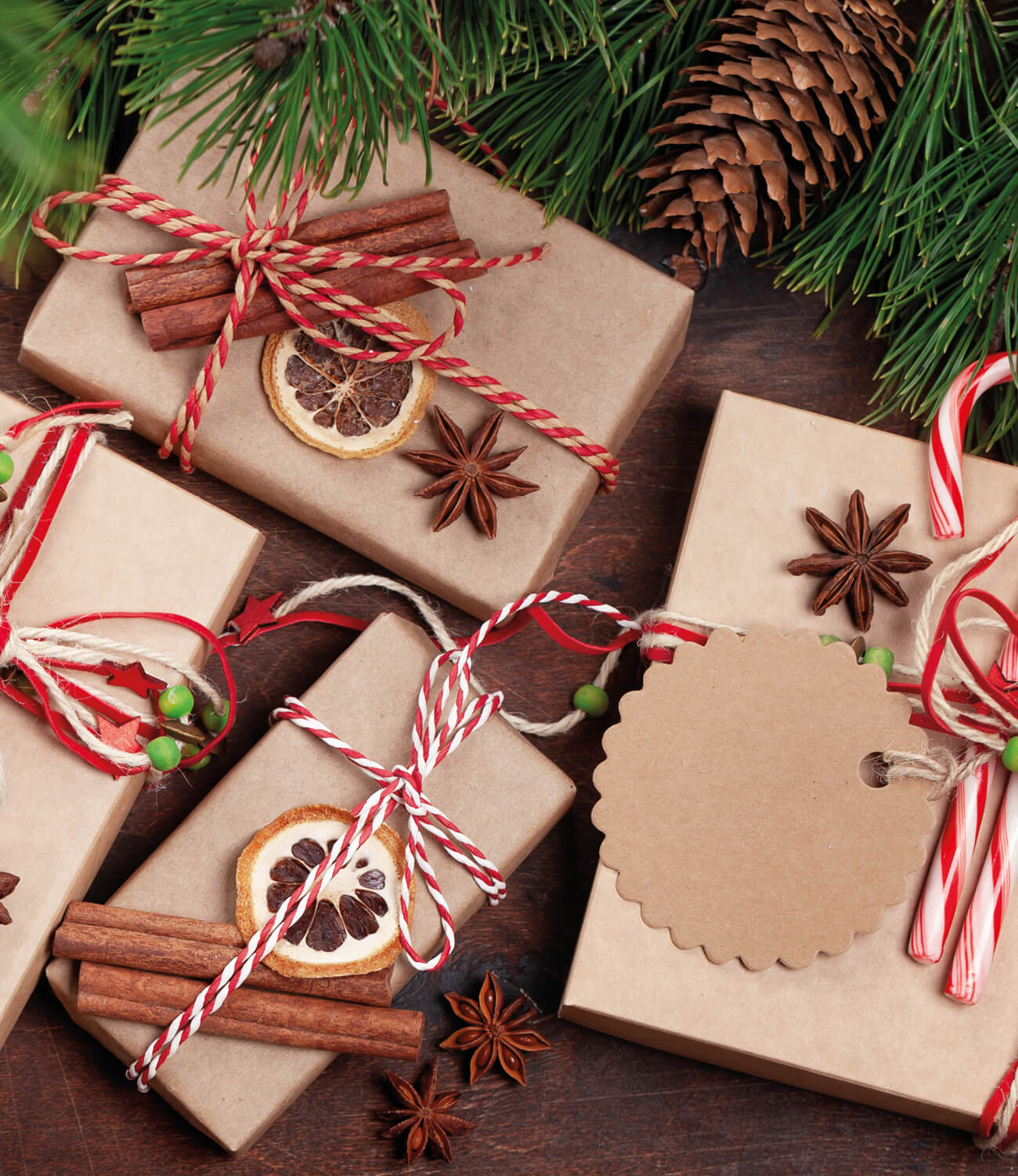 Gift boxes wrapped in brown paper with string, cinnamon sticks, and star anise on a wooden surface with Christmas decorations.