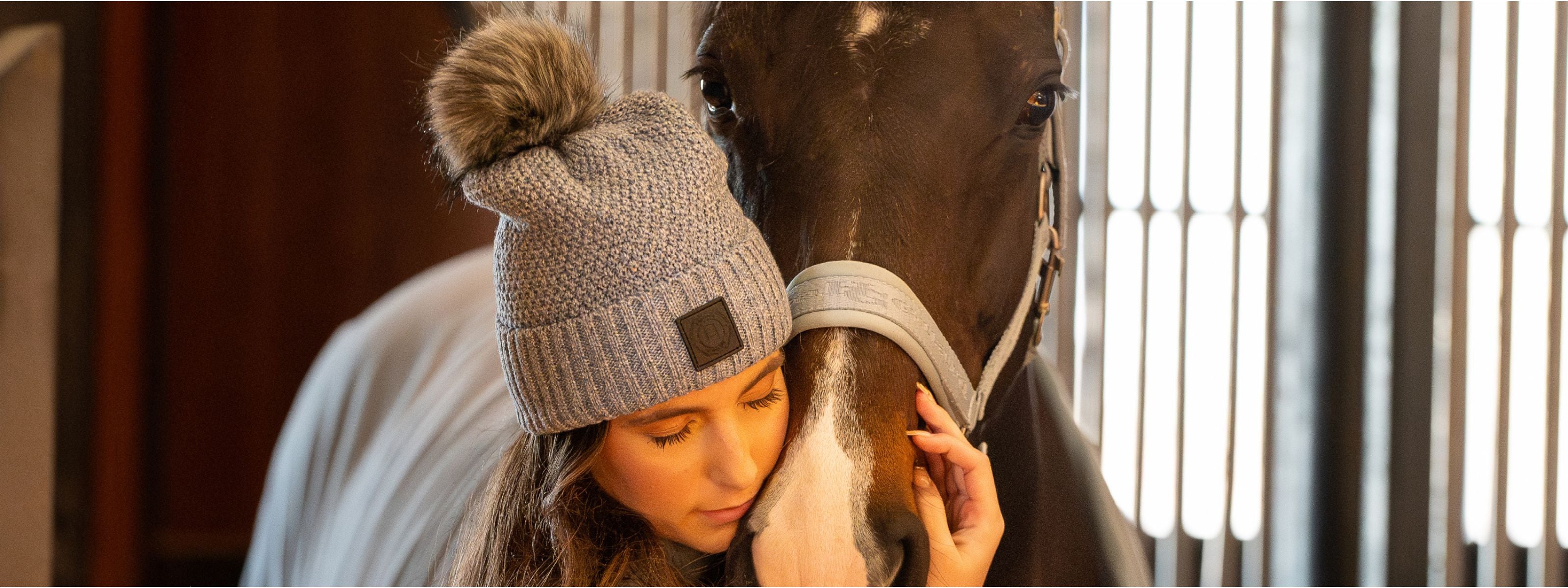 Person wearing a knit hat with a horse in a stable